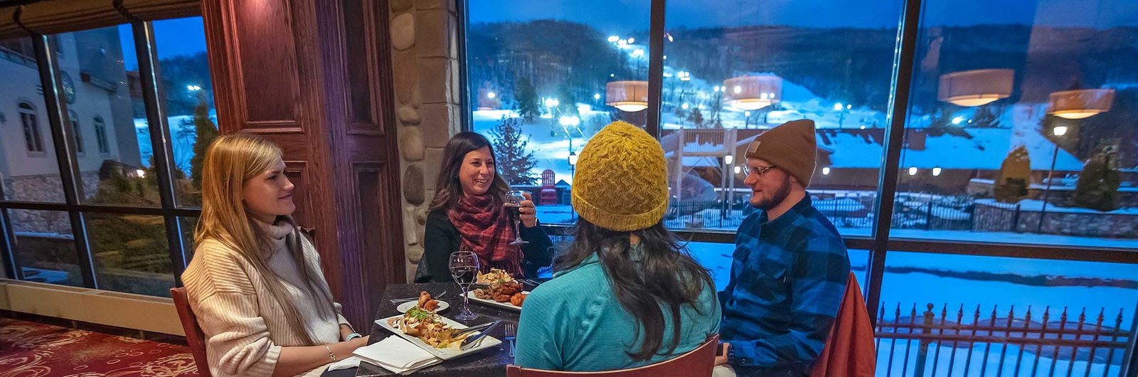 Four people eating at John Harvard's with the ski slopes in the background