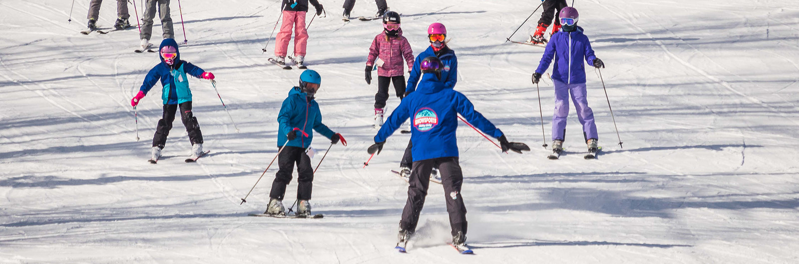 Ski instructor skiing backwards watching a group of kids in a lesson.