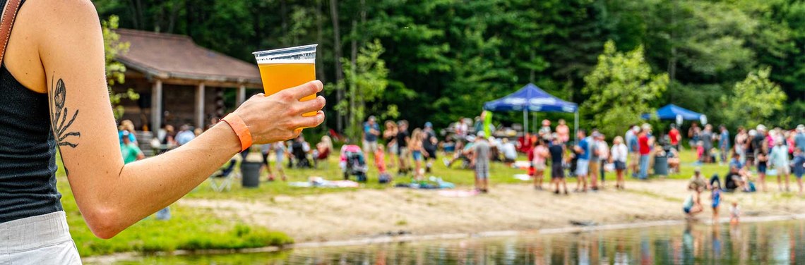 Woman holding a drink looking out at a crowd of people around Spruce Lake.
