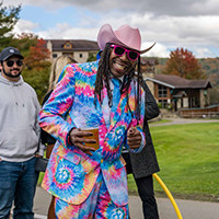 A man in a very vibrant and colorful suit with matching cowboy hat poses for a picture at Fall Festival
