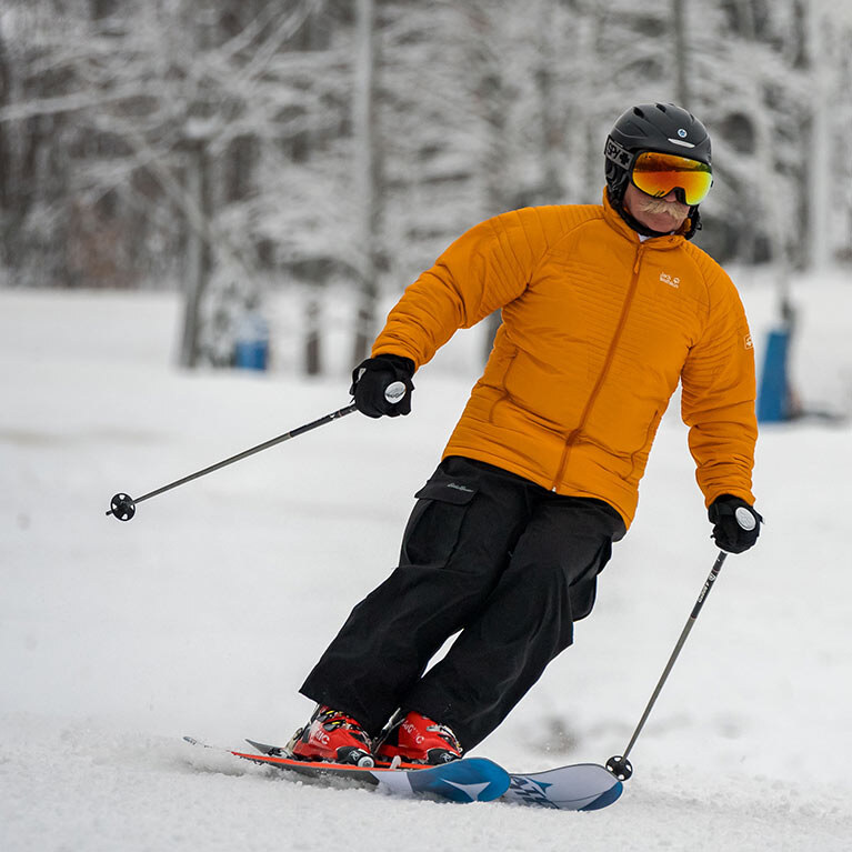 A skier in a bright orange jacket makes his way down a snow filled slope.