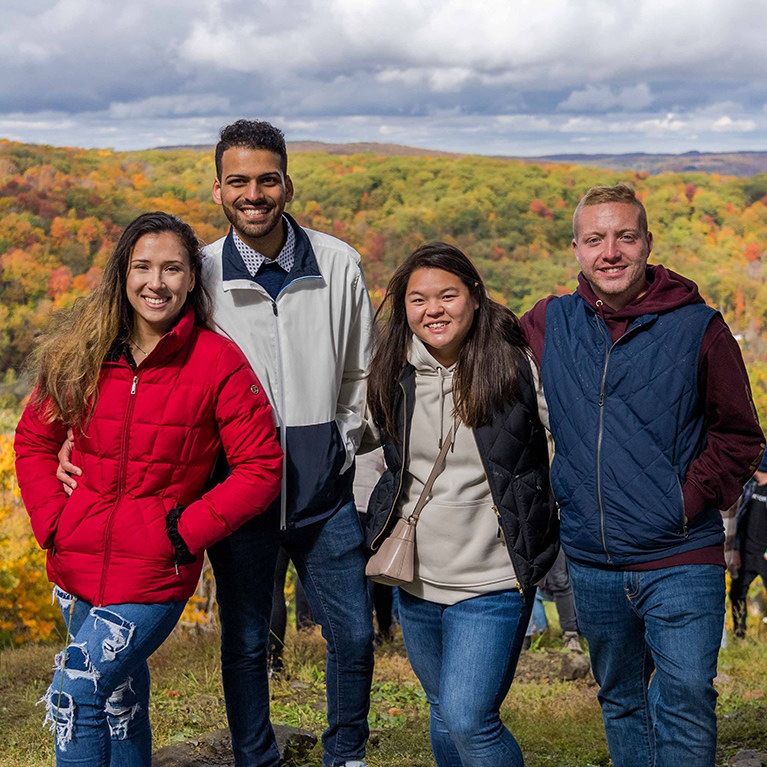 Two couples pose for a photo with a beautiful scene of fall leaves in the background