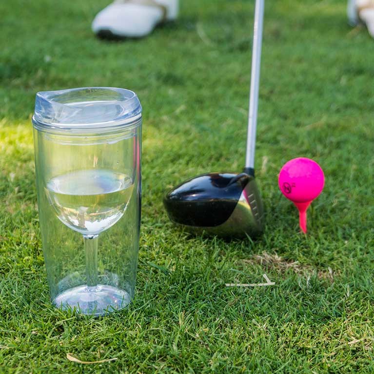 A golf club next to a pink golf ball and a glass of wine.