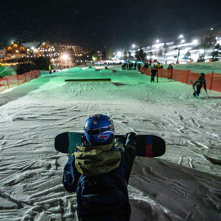 Snowboarder sitting at the top of the rail park, looking at the course.