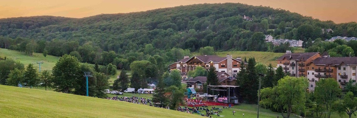A large crowd gathers in the valley in front of a stage to listen to music during the Summer Music Festival