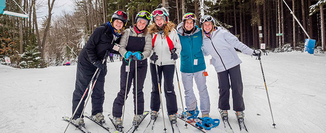A group of five skiers standing together at the top of a hill.
