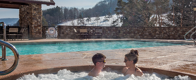 A couple sitting in a hot tub on a sunny winter day.