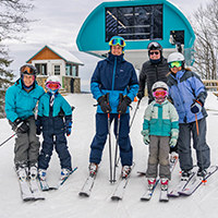 A small group of six skiers standing together at the top of a chairlift.