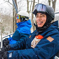 A father and smiling son are riding on a chairlift.