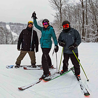 Two skiers and a snowboarder standing at the top of a slope, posing for a picture.