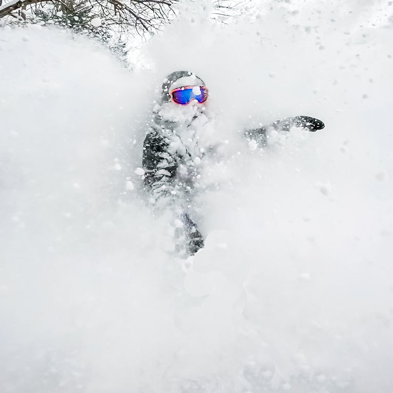 A closeup view of a snowboarder coming out of a cloud of powder.