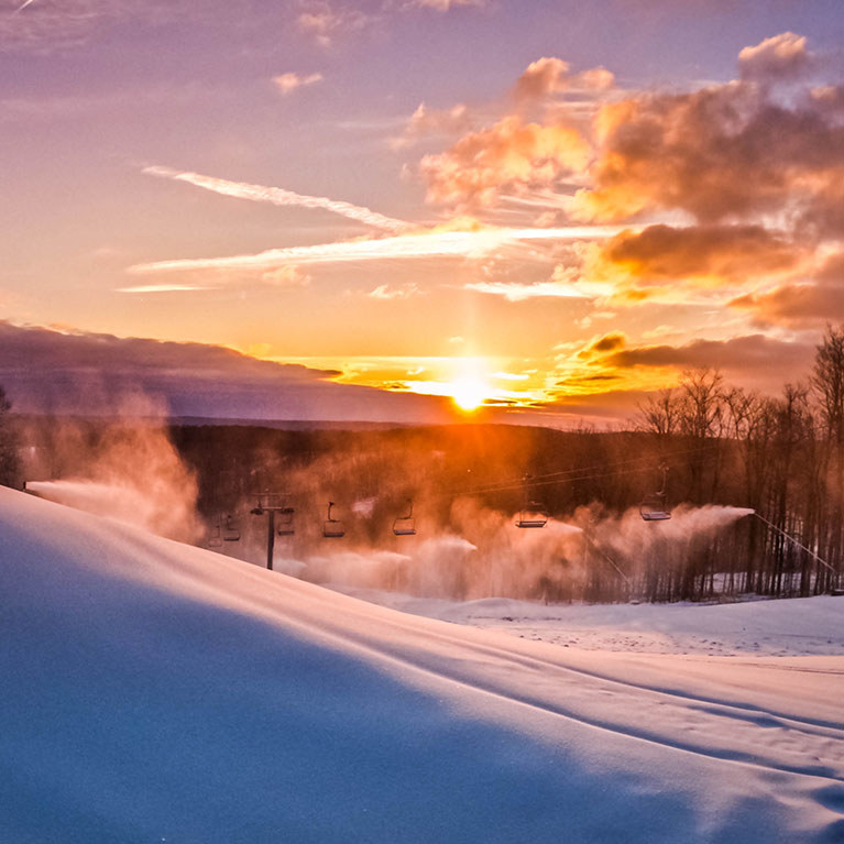 An early morning sunrise with snowmaking guns making snow on a hill.