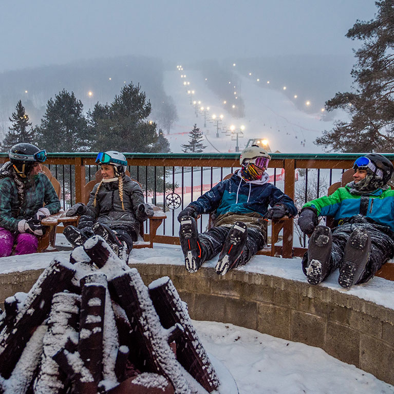 College age skiers talking and relaxing at bottom of the mountain on a winter night